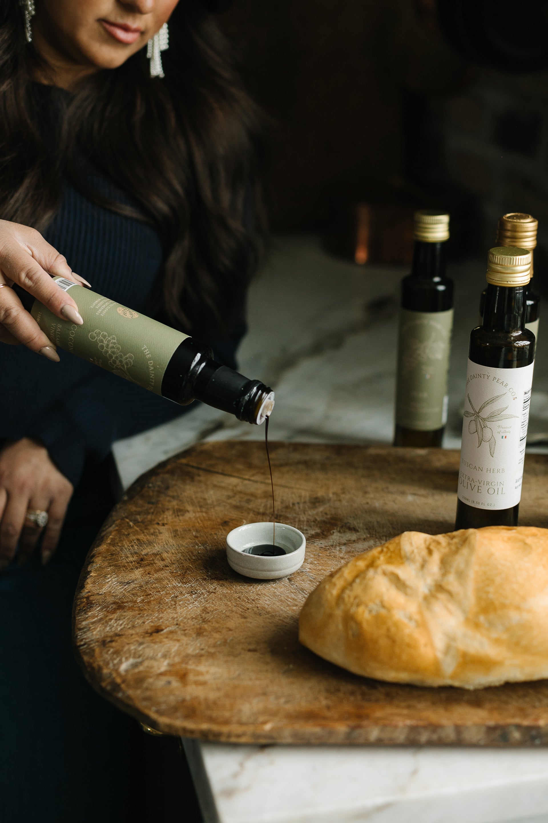 Person pouring olive oil from a bottle onto bread on a wooden board.