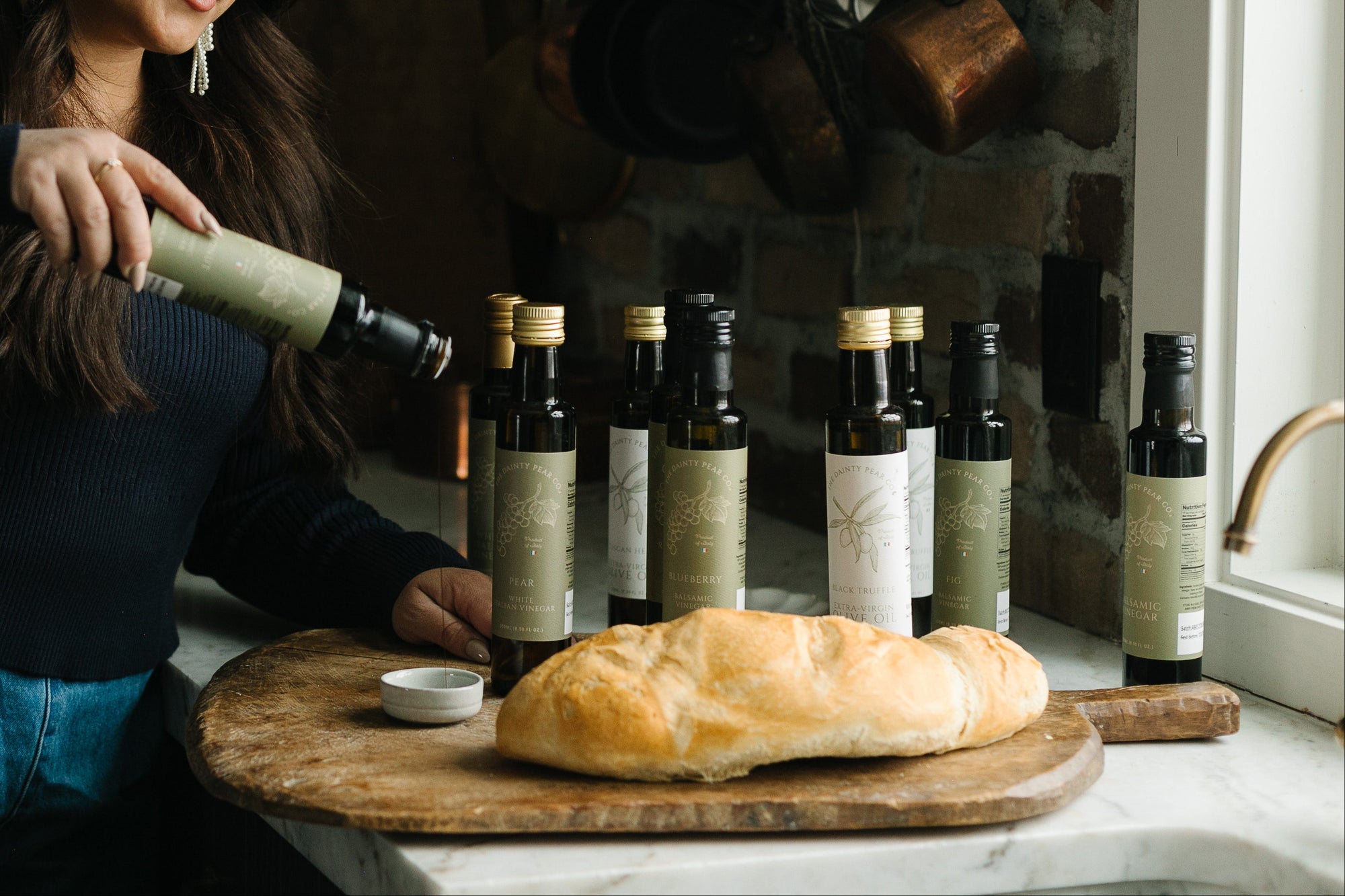 Woman in a kitchen pouring olive oil into a bottle with bread on a cutting board.