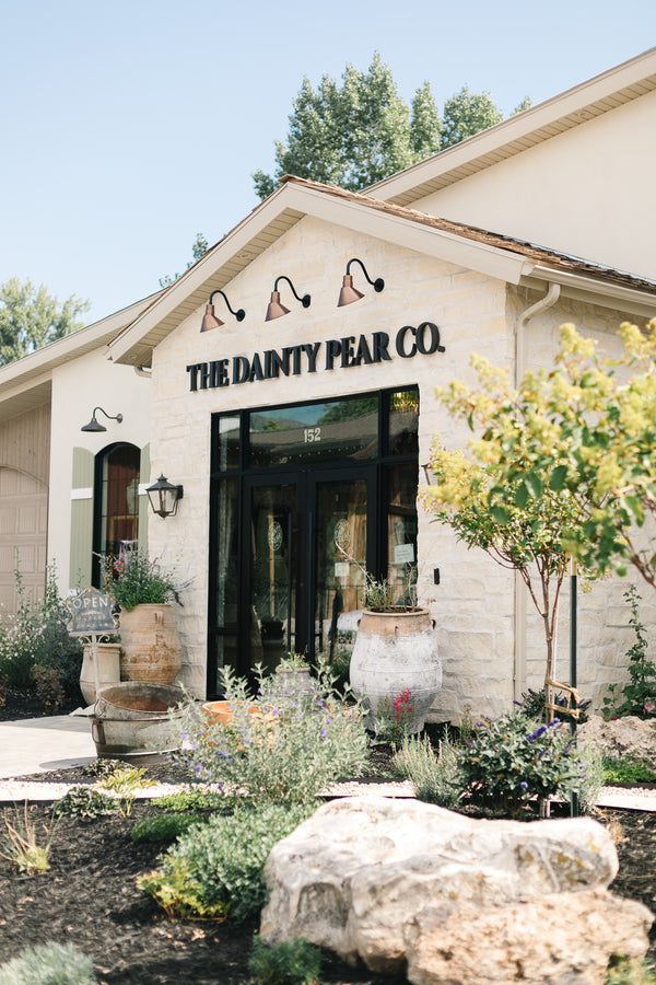 Building with 'The Dainty Pear Co' sign, surrounded by plants and flowers.