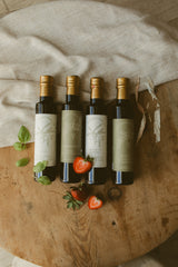 Five bottles of olive oil on a wooden surface with herbs and strawberries.