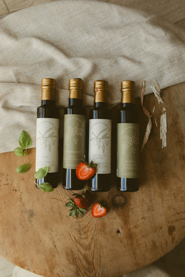 Five bottles of olive oil on a wooden surface with herbs and strawberries.