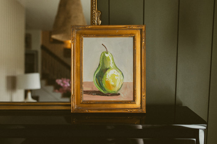 Original oil painting of a single green pear on a blush pink tabletop by Chantry Brewer, in a carved gold frame