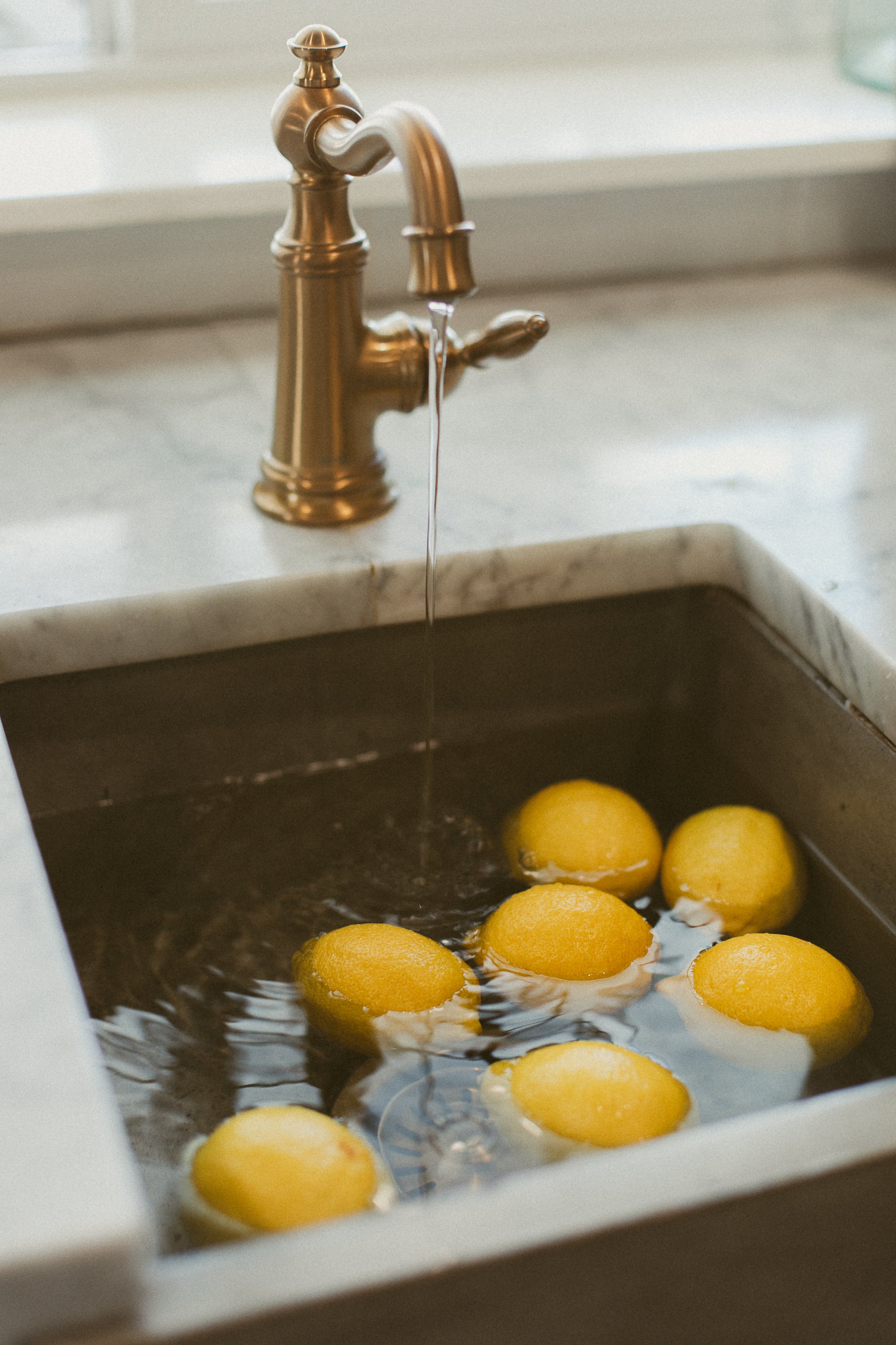 Lemons being washed in a kitchen sink with a gold faucet.